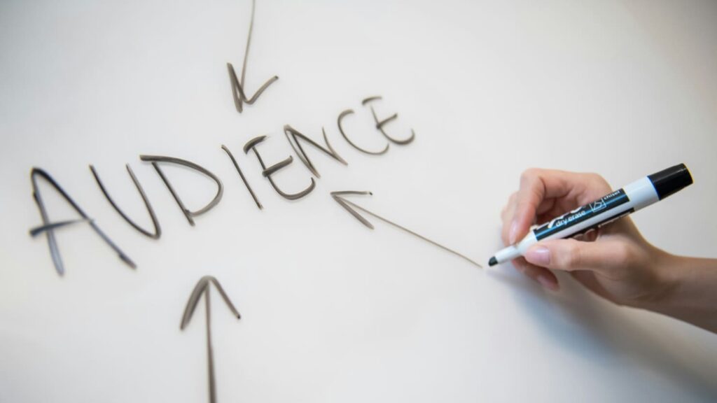 hand writing the word audience on whiteboard